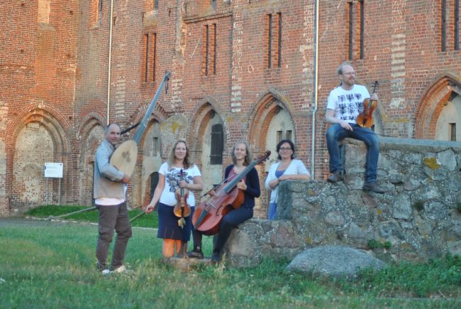 Grupa pięciu muzyków przed gotyckim kościołem z czerwonej cegły